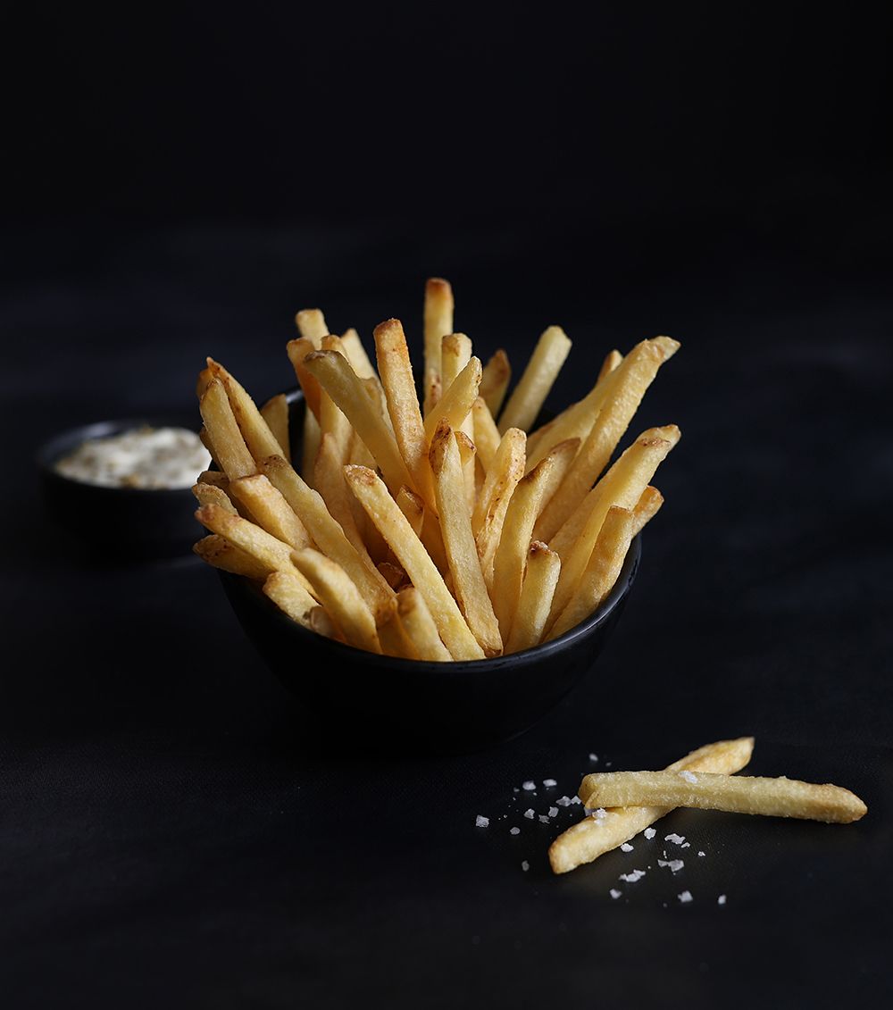 Golden French fries in a black bowl on a dark background, with a few fries scattered nearby.