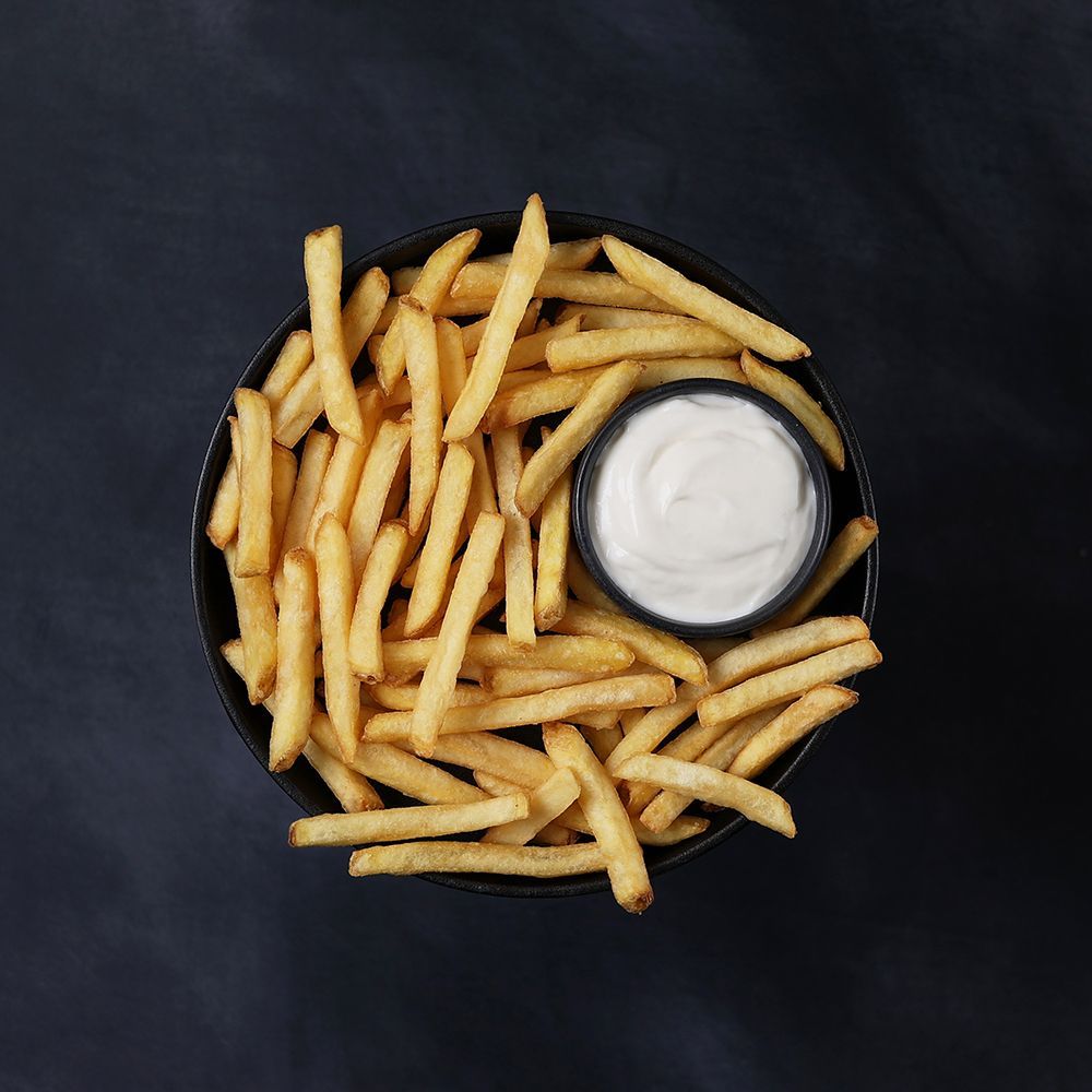 Fries in a black bowl with a cup of white dipping sauce on a dark background