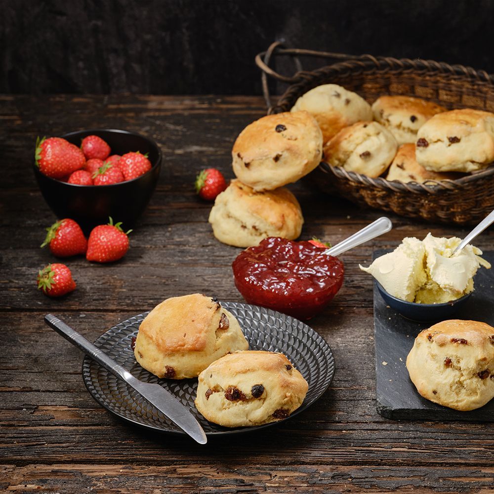 Scones with strawberries, jam, and clotted cream on a rustic wooden table