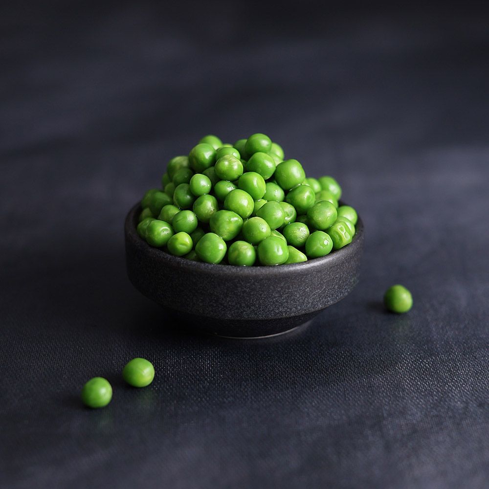 Bowl of green peas on a dark cloth, with a few peas scattered nearby