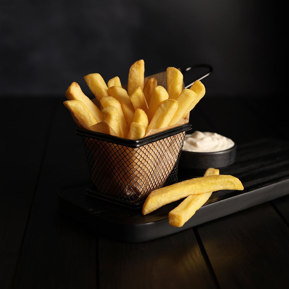 Golden French fries in a wire basket with dipping sauce on a dark table