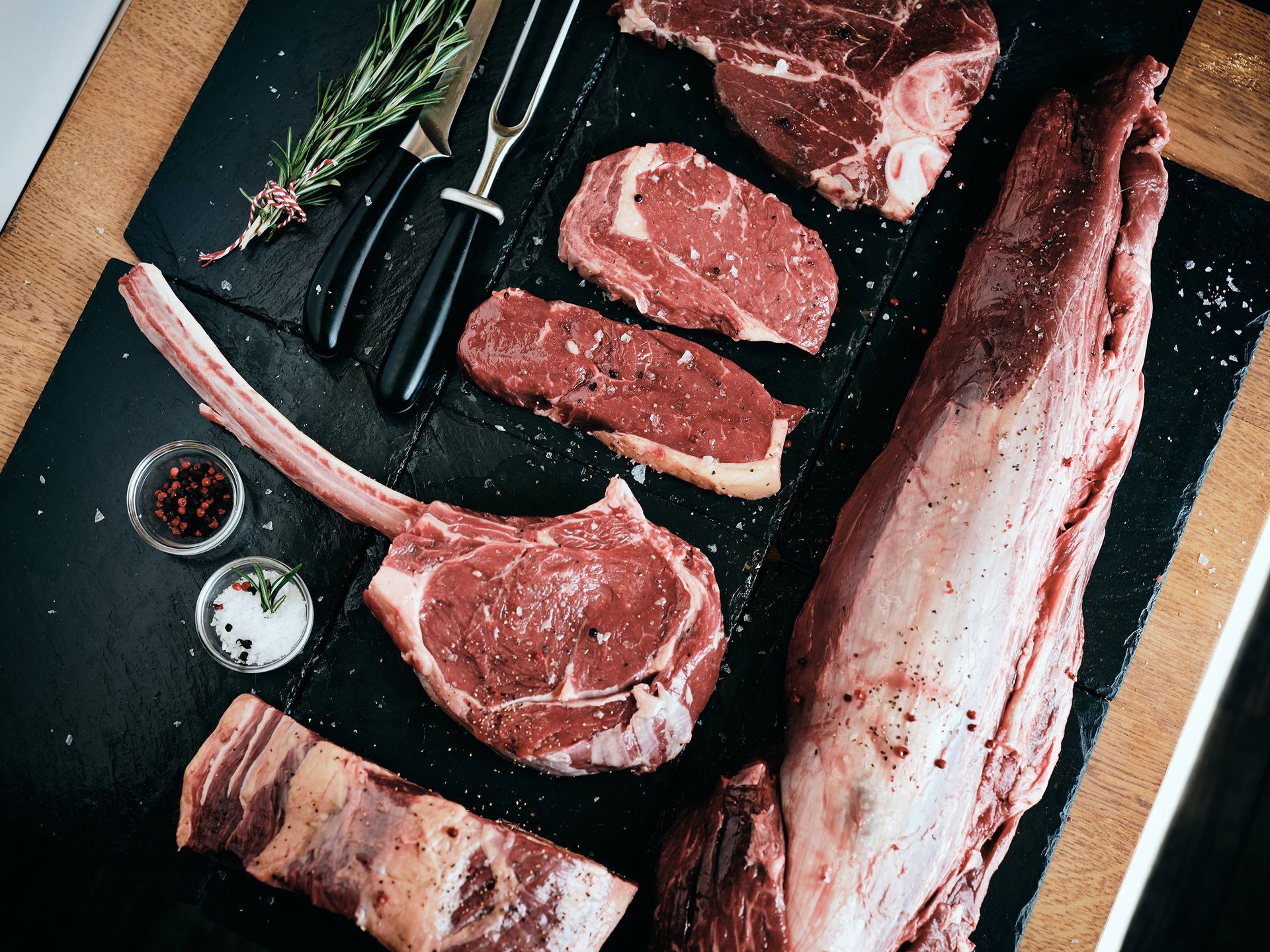 Raw steaks and cuts of meat on a cutting board with herbs and seasoning on the side