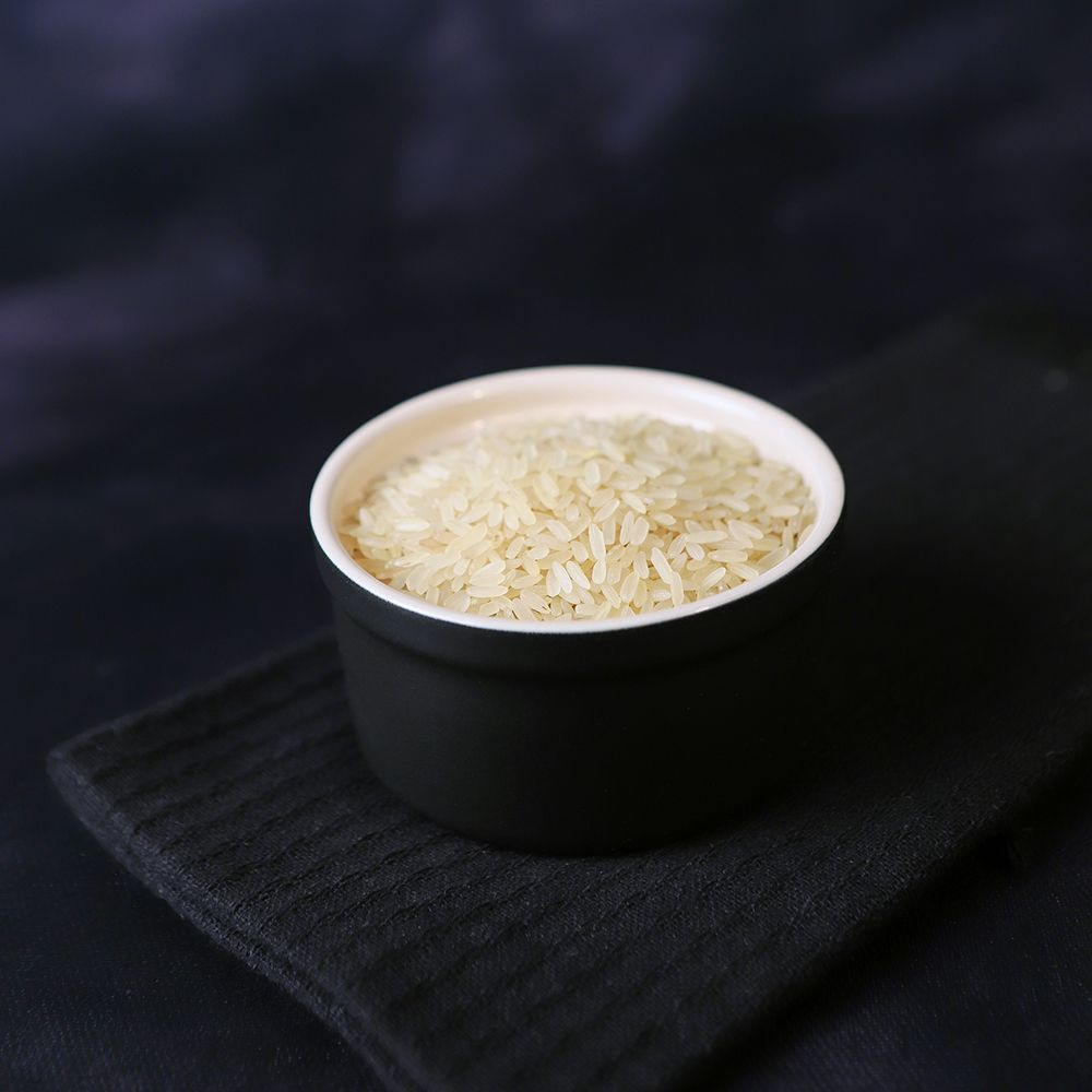 Small black cup filled with rice on a black napkin against a dark background