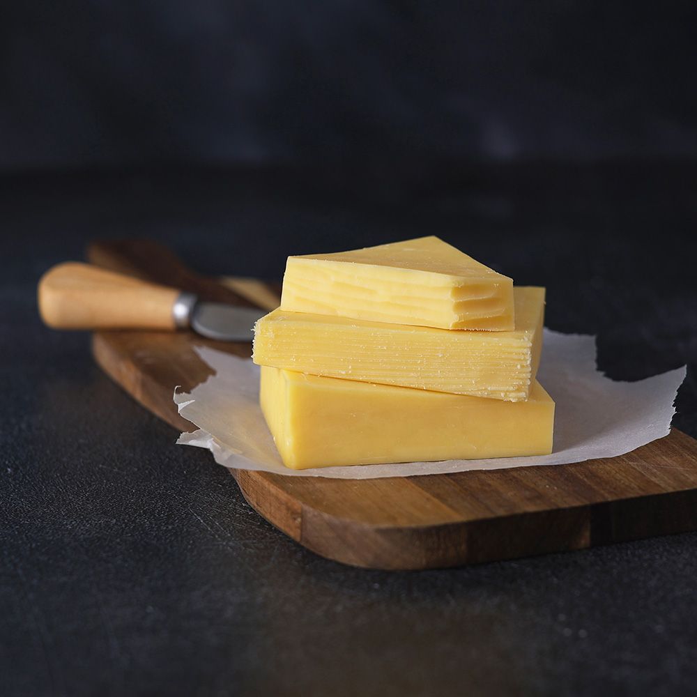 Butter yellow cheese slices stacked on parchment atop a wooden board with a knife handle visible
