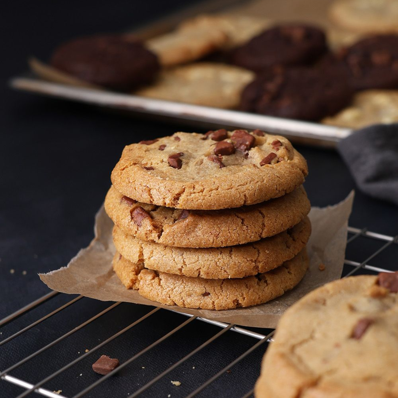 Stack of chocolate chip cookies on parchment paper, with more cookies blurred in the background