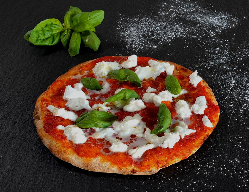 Margherita pizza with basil and melted cheese on a dark surface, with fresh basil nearby