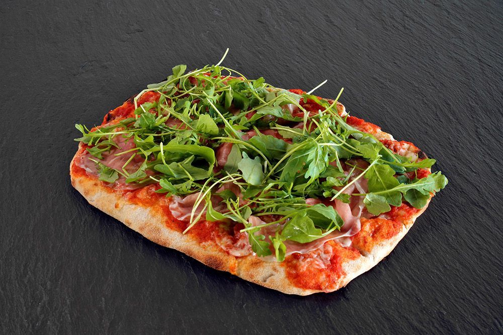 Rectangular pizza topped with greens and red sauce on a dark slate surface
