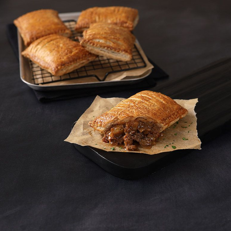 Tray of golden pastries, one cut open to show filling on parchment paper against a dark background