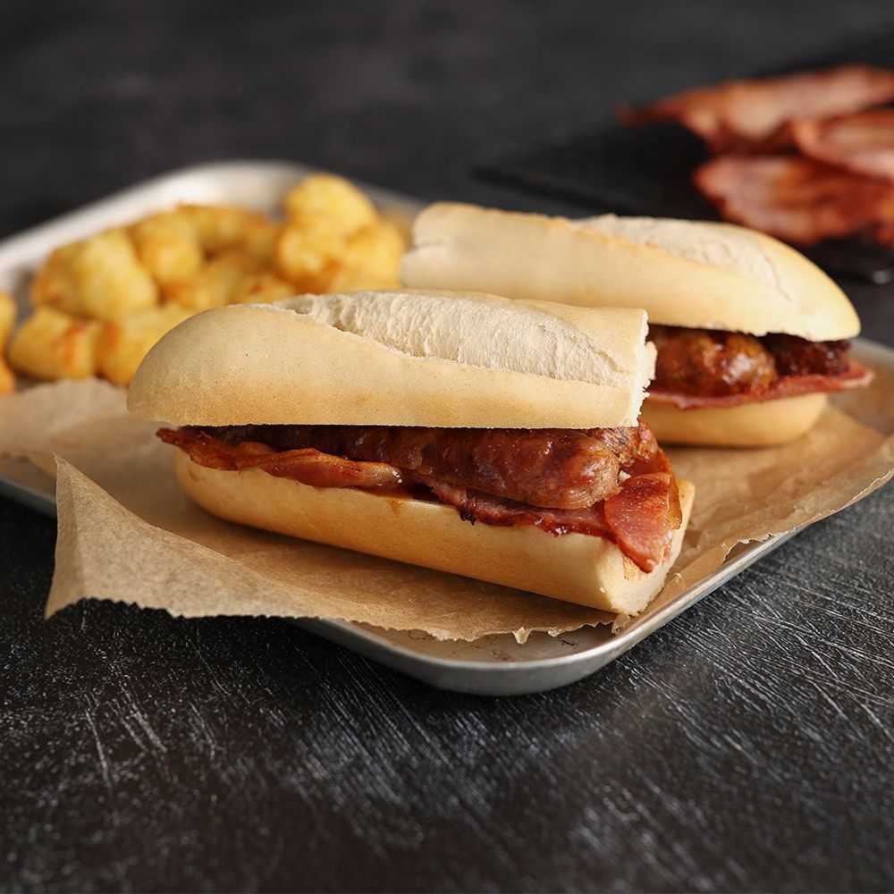 Two sandwiches with bacon on parchment, served with tater tots on a tray against a dark background