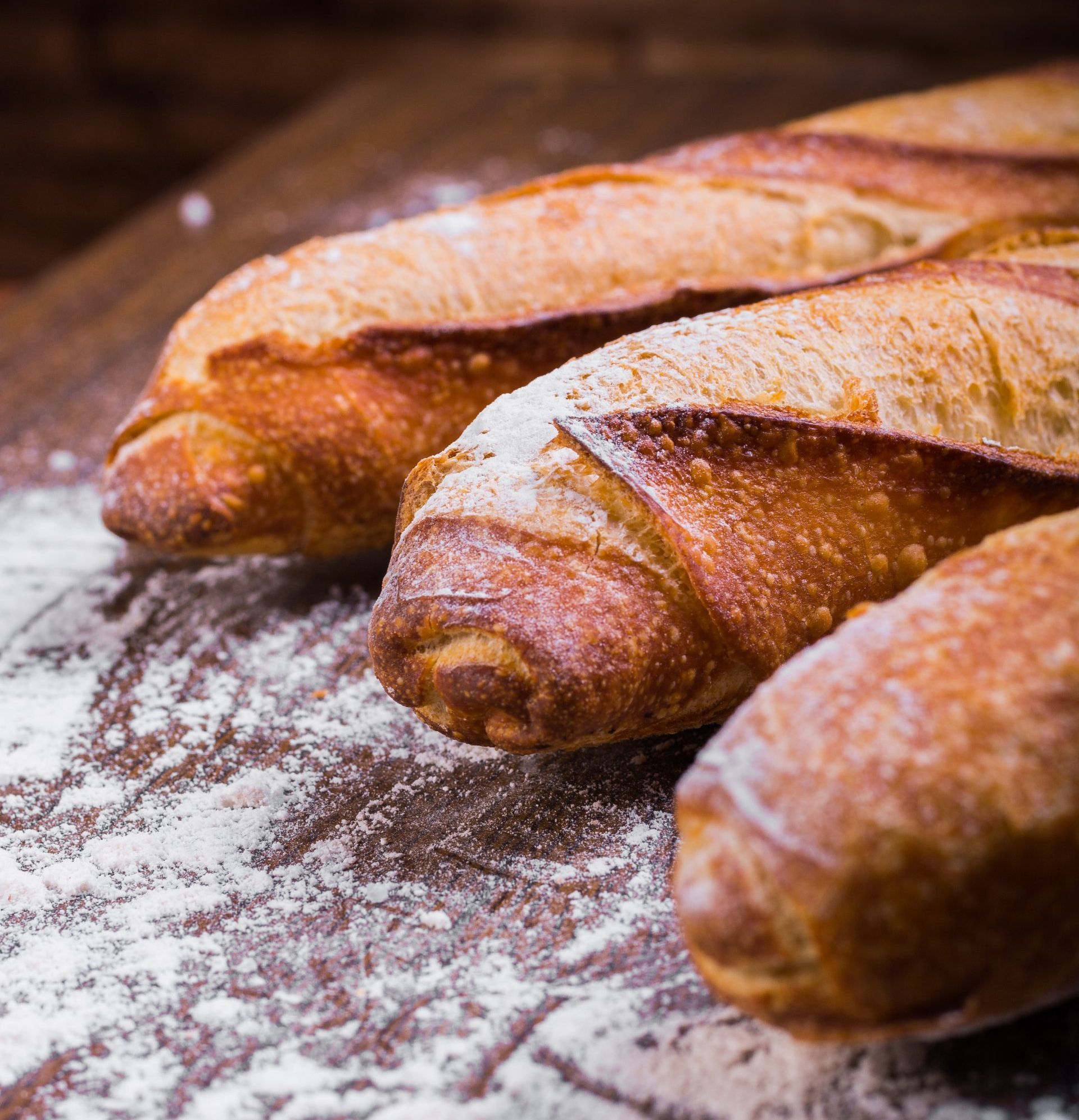 Three crusty baguettes dusted with flour on a wooden table
