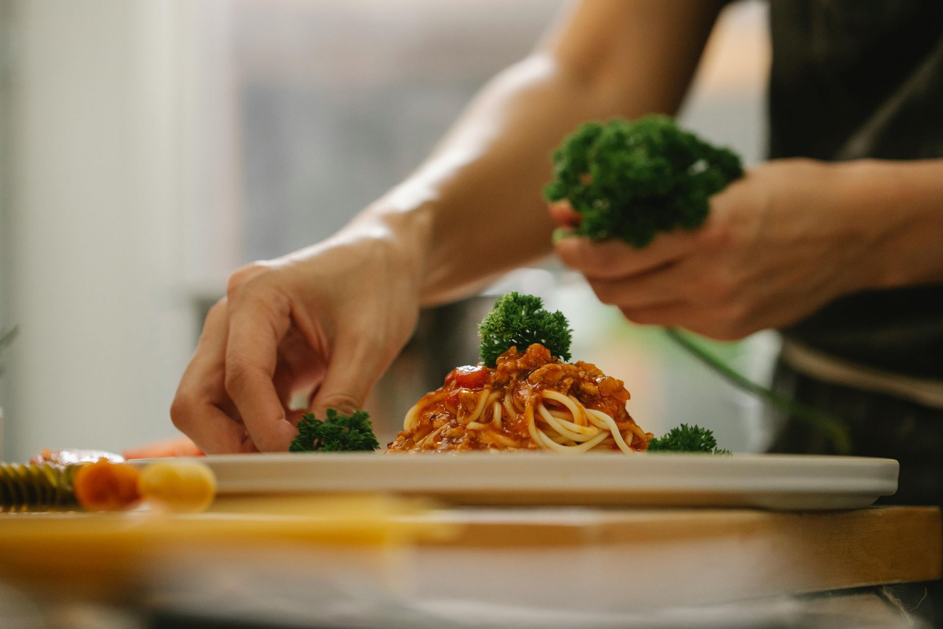 Hands plating spaghetti with broccoli on a white dish in a kitchen