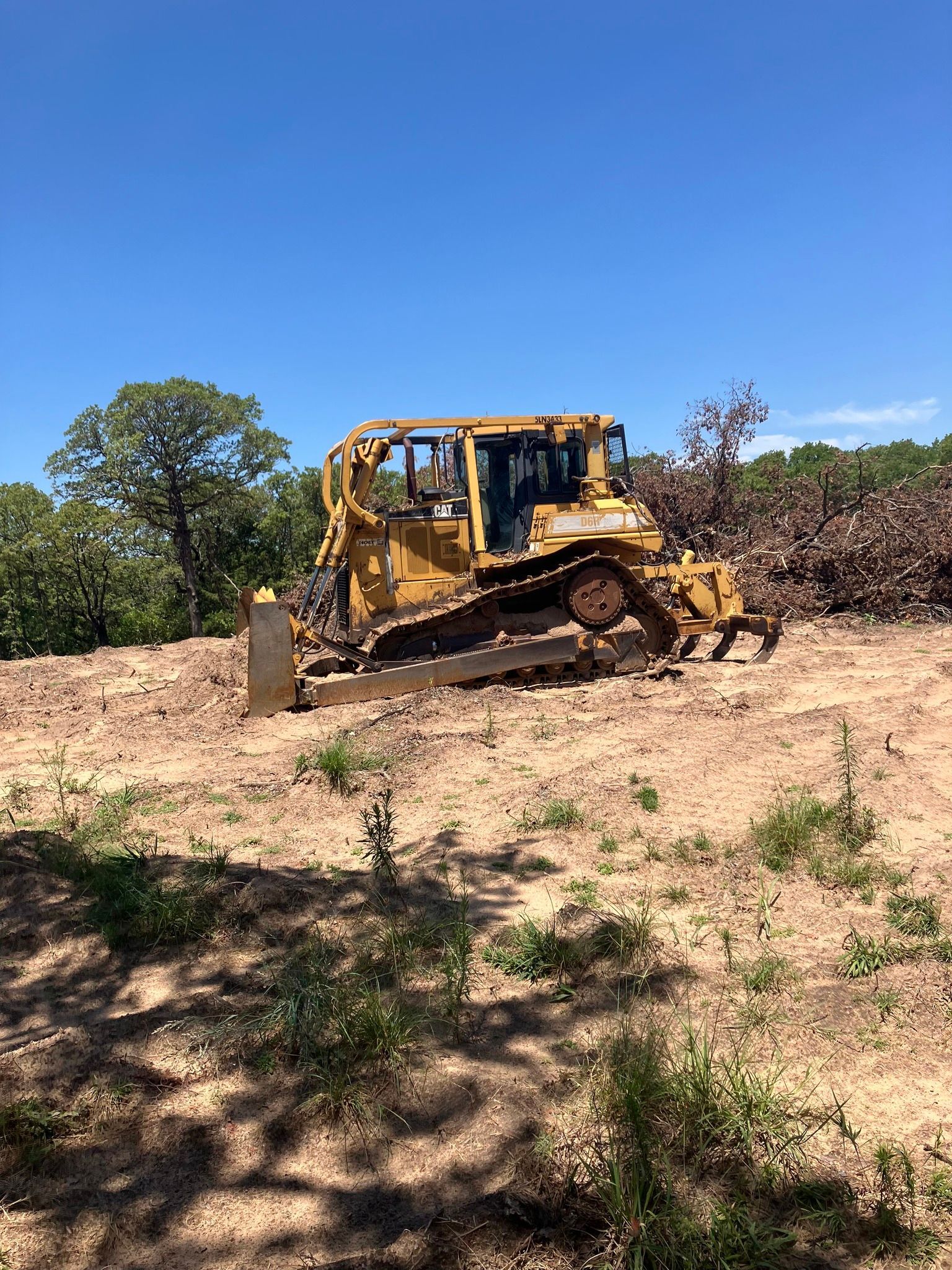 Yellow bulldozer clearing dry dirt on a hillside under a bright blue sky