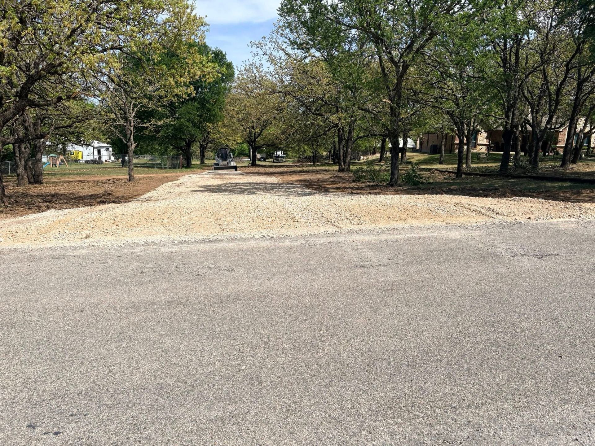 Paved road beside a dirt turnout and trees in a park-like area