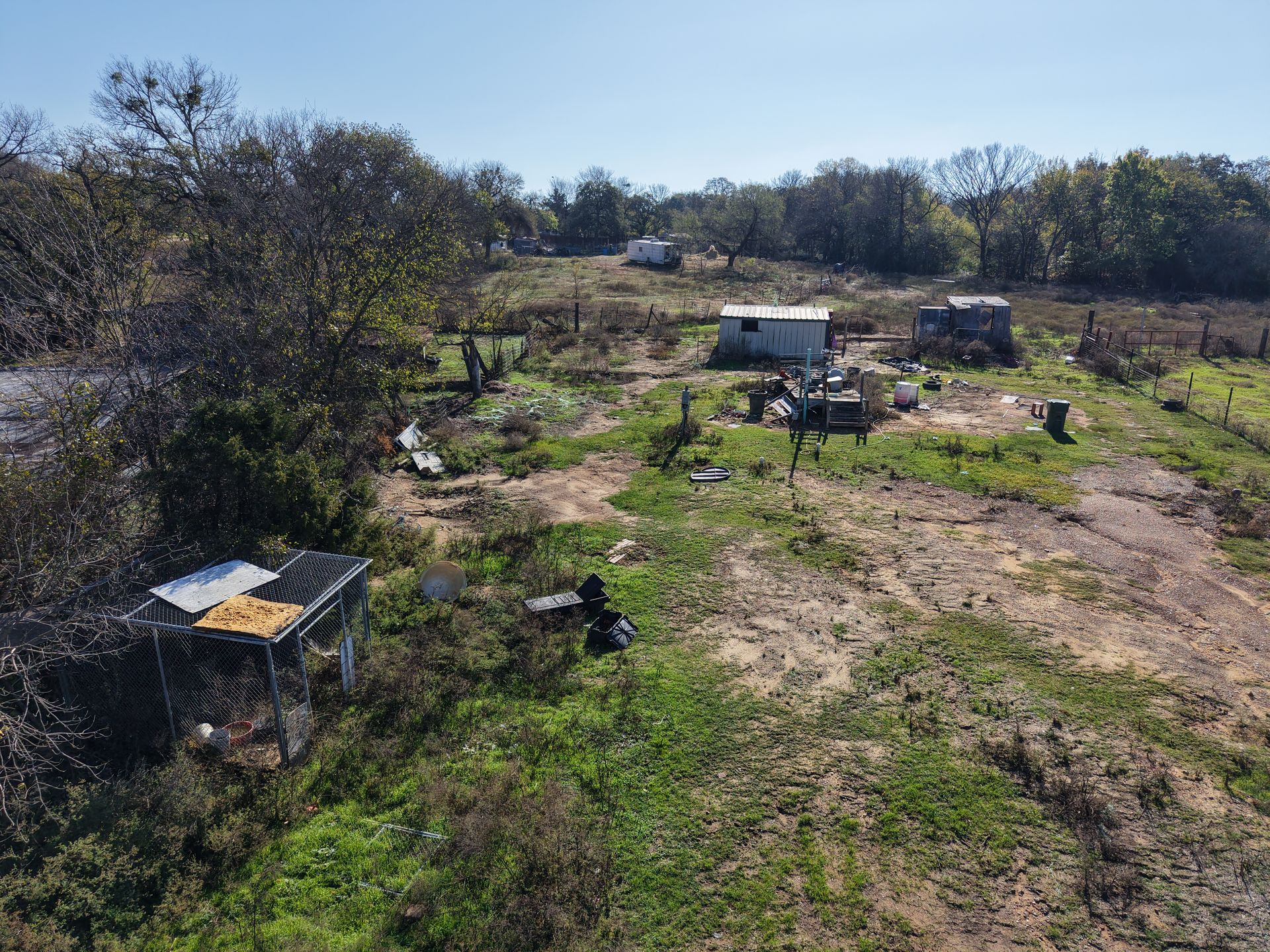Rural field with scattered vehicles and equipment under a clear sky, viewed from a dirt path