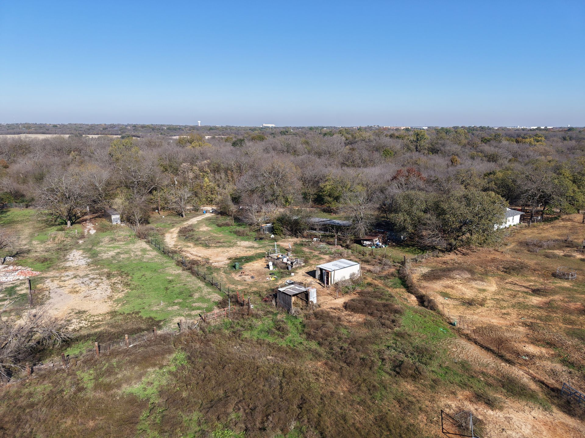 Dry scrubland with scattered trees and a small white structure under a clear blue sky