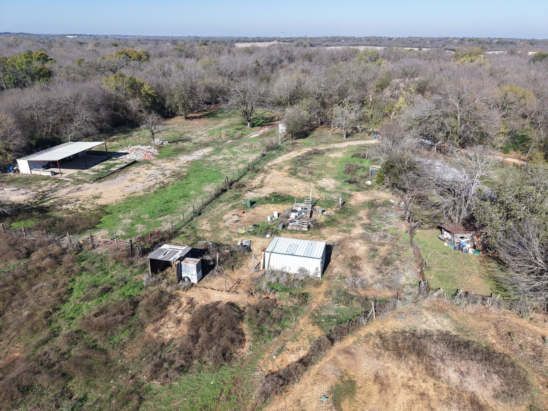 Aerial view of a dry rural field with scattered small sheds, dirt paths, and sparse trees.