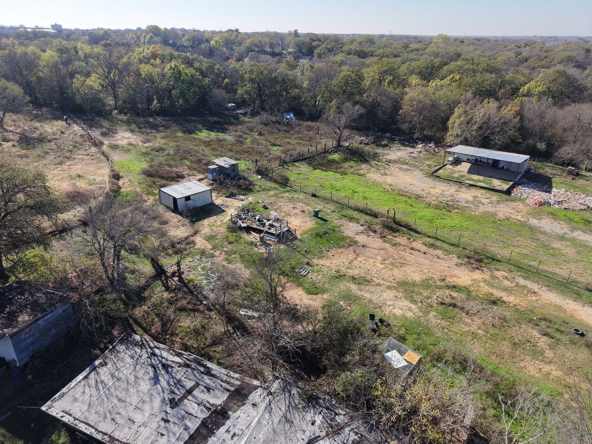 Aerial view of a rural property with small buildings, dirt tracks, and green fields surrounded by trees