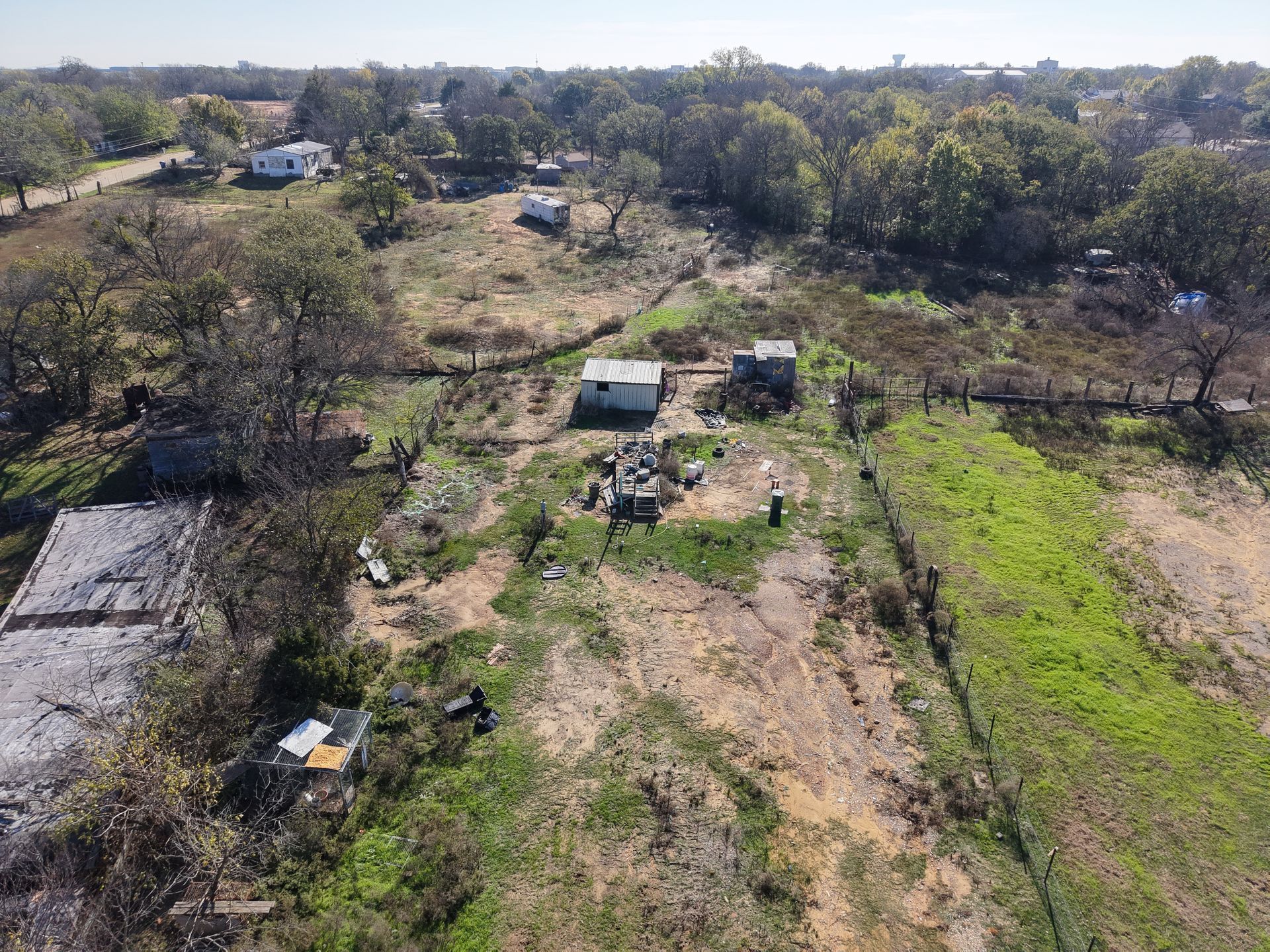 Aerial view of a rural property with scattered trees, dirt paths, and small buildings.