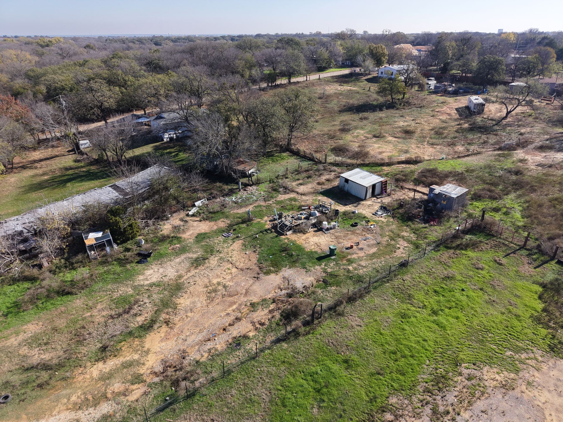 Aerial view of a rural area with scattered trees, dirt paths, and a few small buildings.