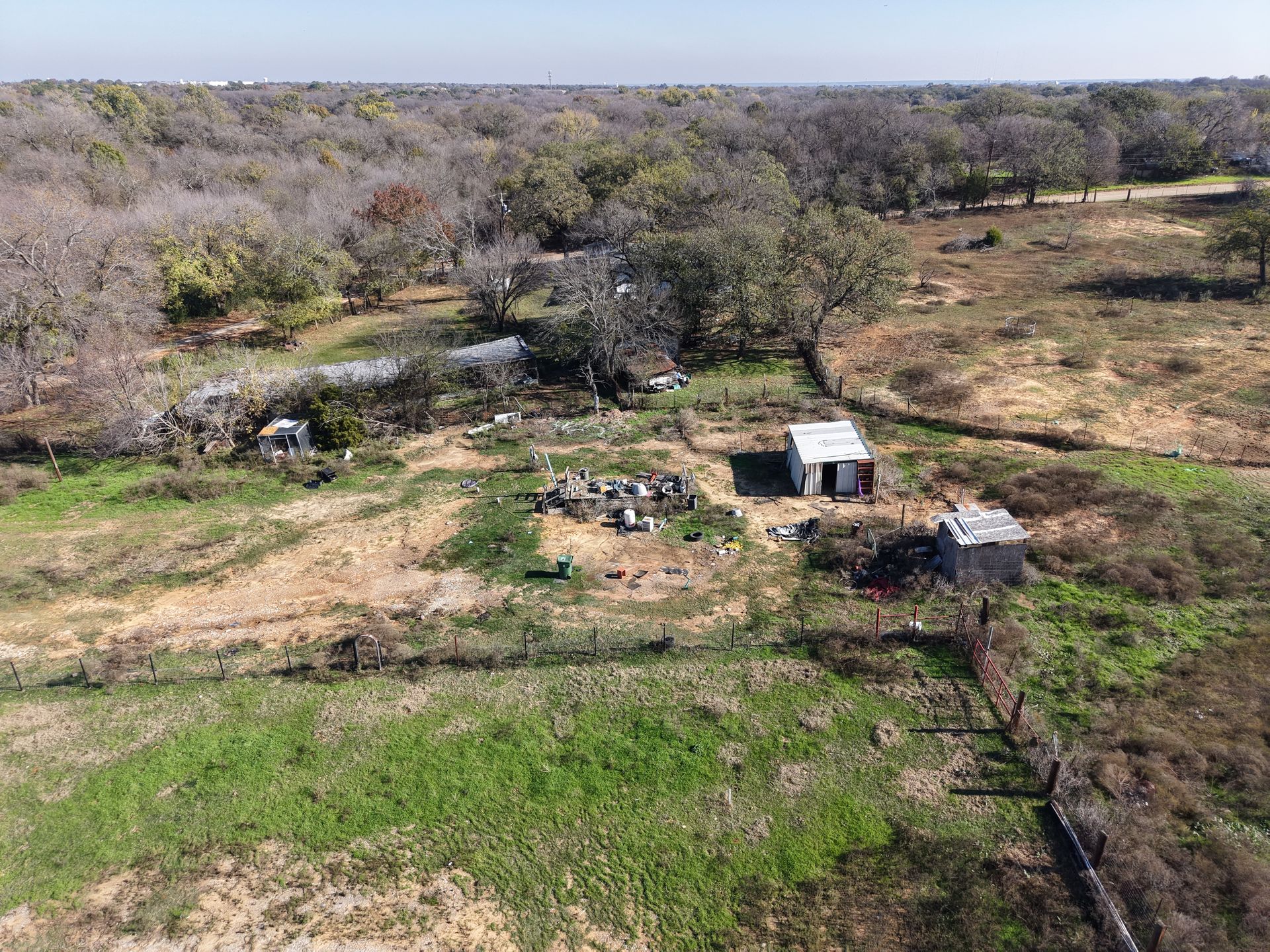 Aerial view of a rural homestead with small buildings, bare trees, and green fields.