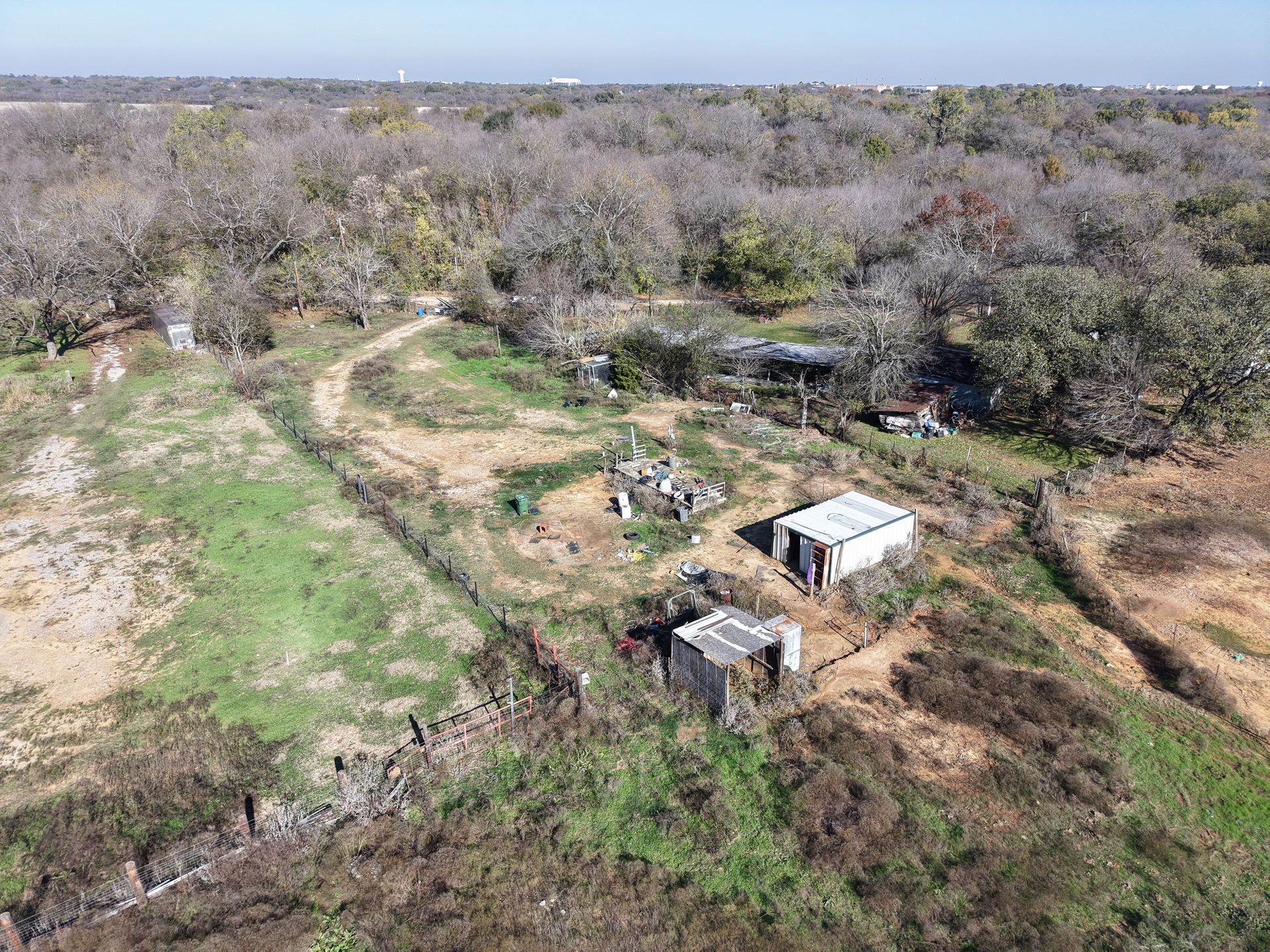 Aerial view of a dry, wooded area with a dirt path and two small sheds.