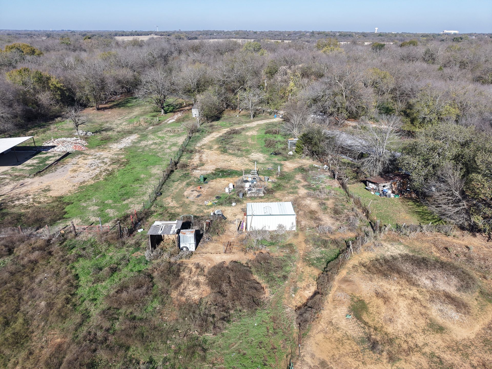 Aerial view of a dry, brushy landscape with dirt tracks, small structures, and scattered trees