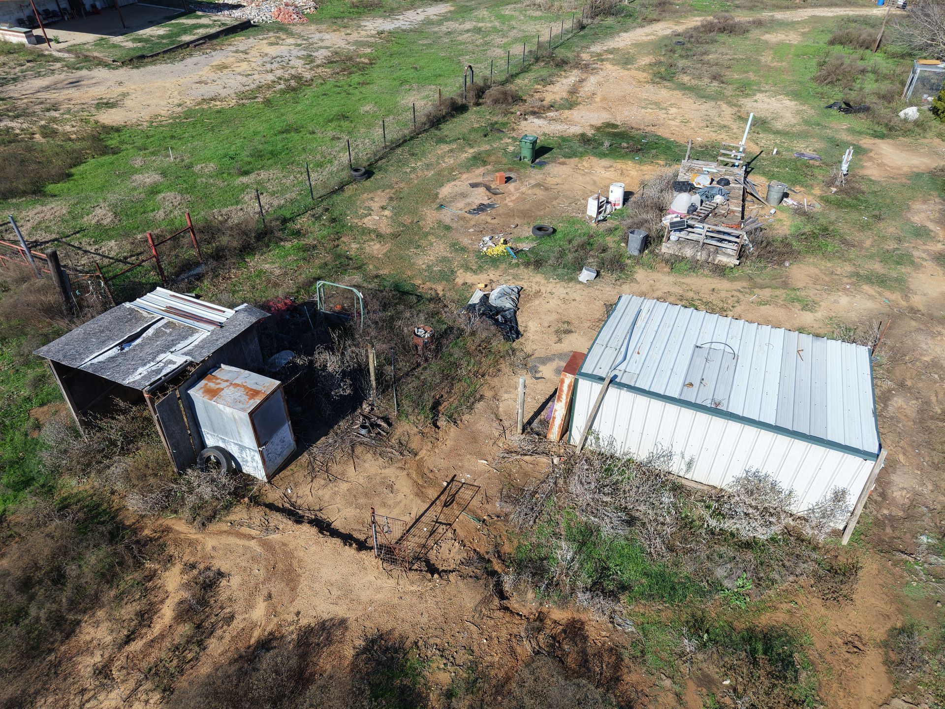 Aerial view of a rural yard with two small sheds, dirt paths, and scattered debris.