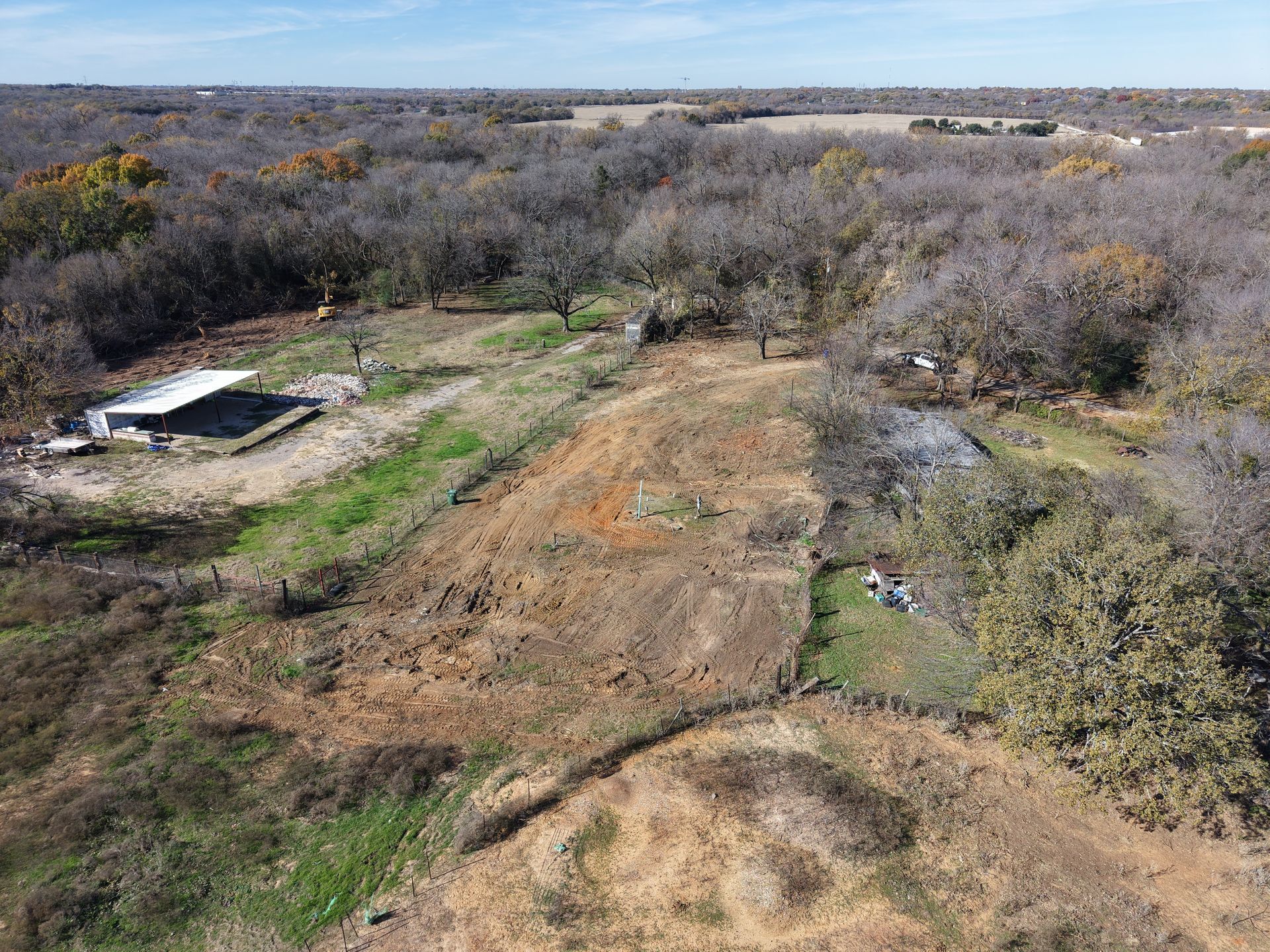 Aerial view of a rural field with dirt paths, leafless trees, and a small shed under a cloudy sky