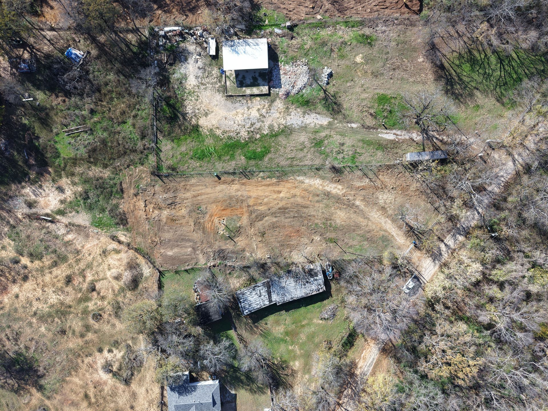 Aerial view of a rural hillside with scattered small buildings, dirt paths, and dry vegetation.