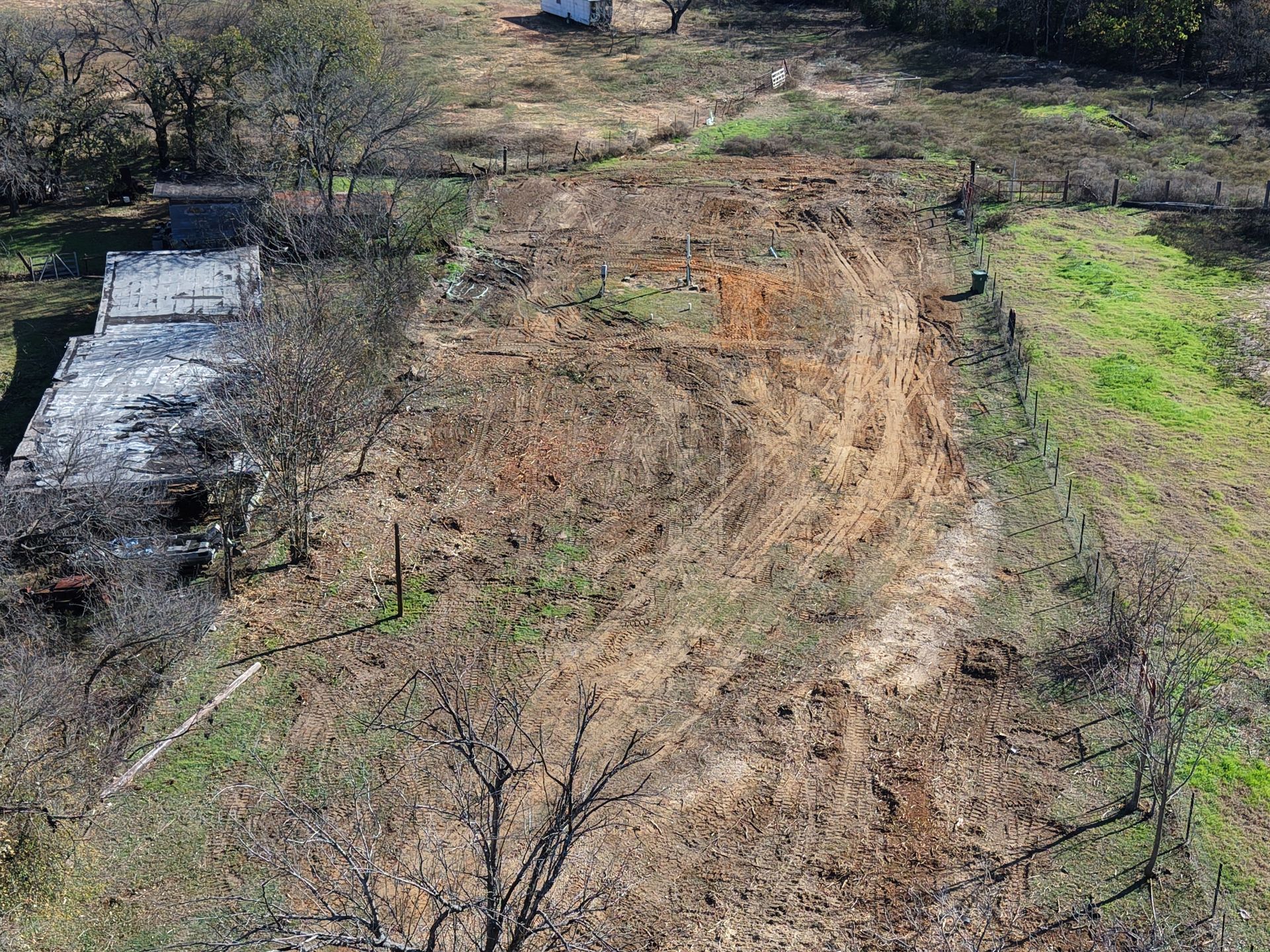 Dry dirt field with tire tracks, sparse trees, and a small concrete water structure on the left