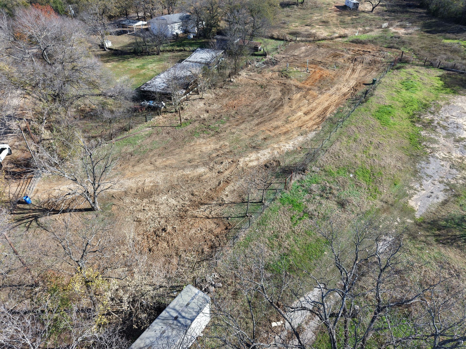 A dry, grassy hillside with scattered trees, patches of green, and a small creek or drainage channel.