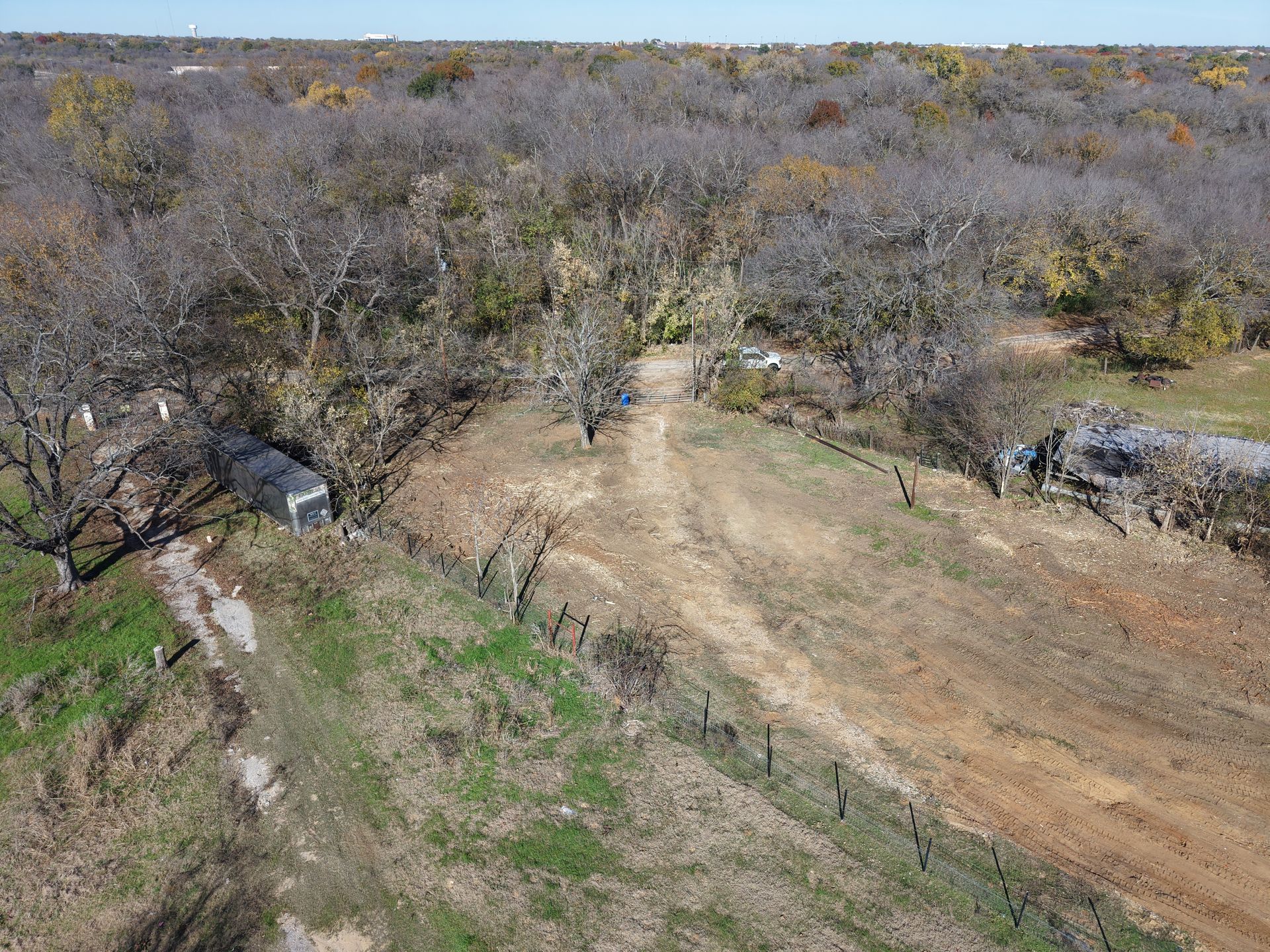 Dry, wooded landscape with a dirt road and sparse green patches under a gray sky