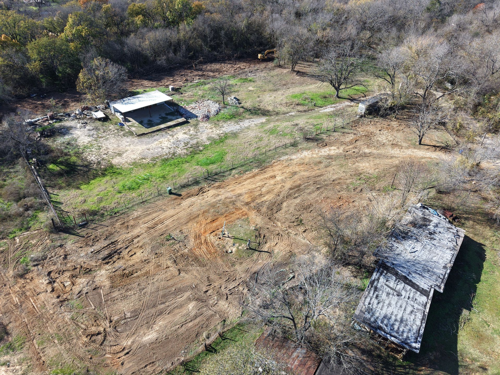 Aerial view of a dry rural field with two small buildings and sparse trees.