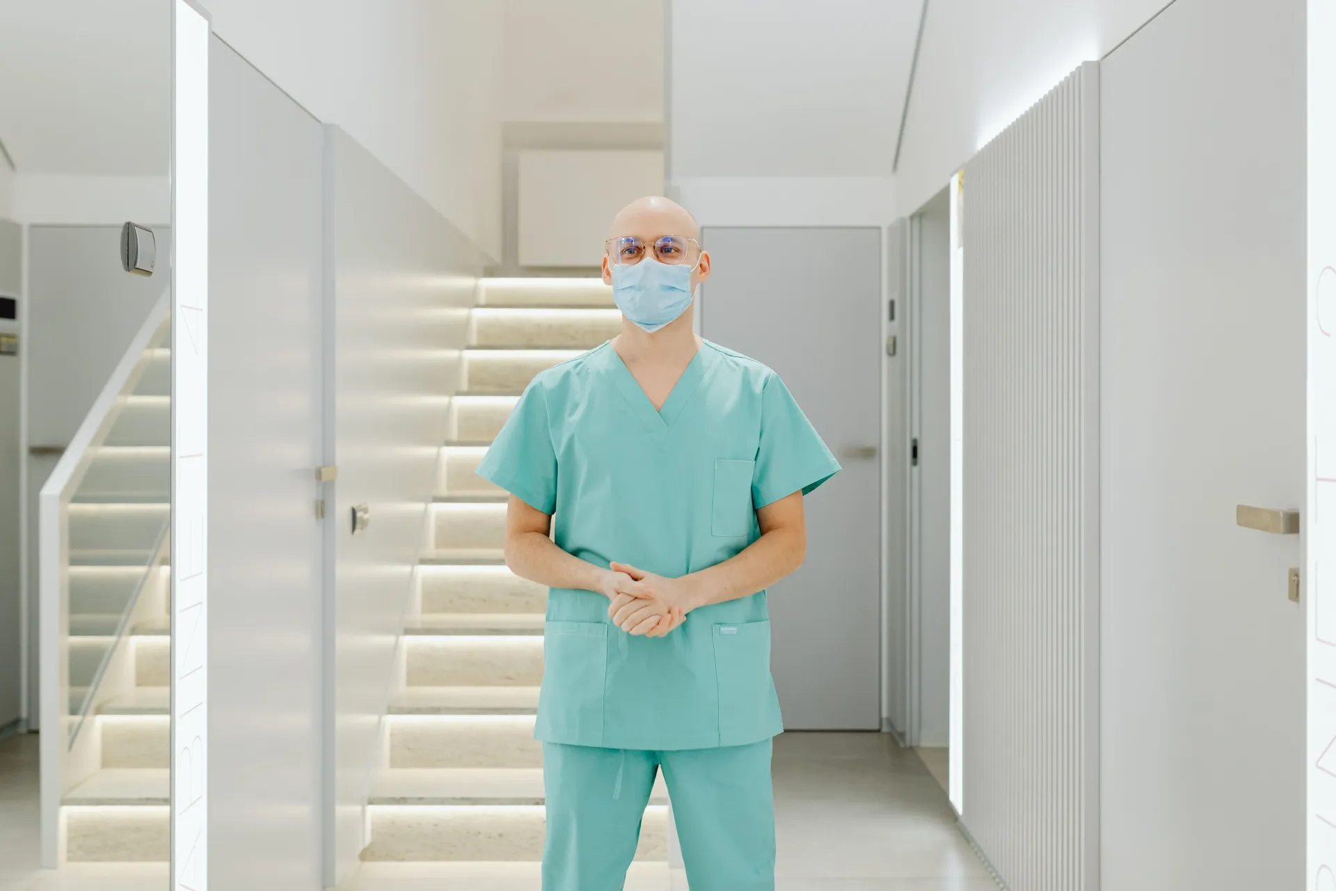 Medical professional in teal scrubs and mask standing in a bright hallway