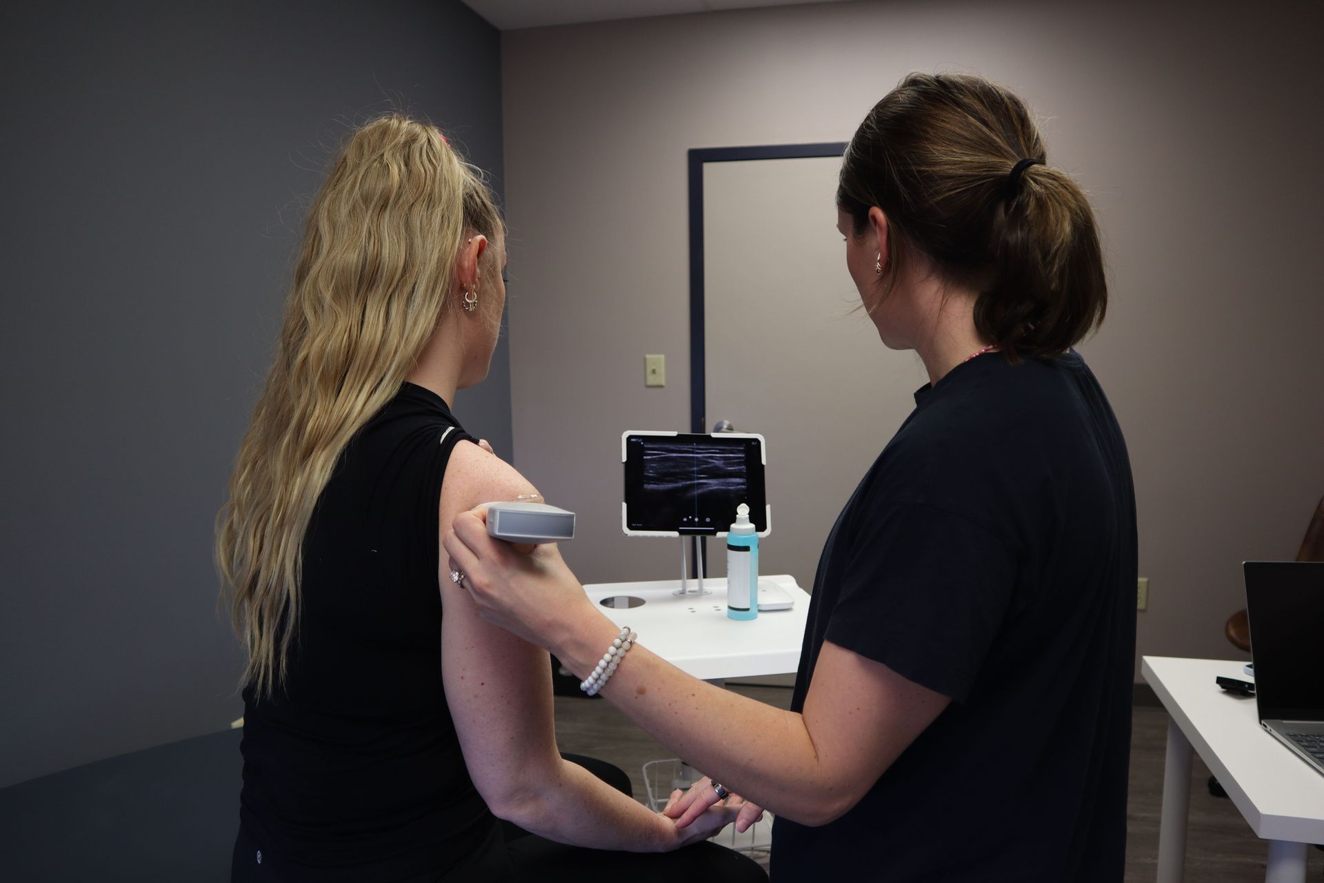Clinician scans a patient’s upper arm in a medical exam room while a monitor displays results.