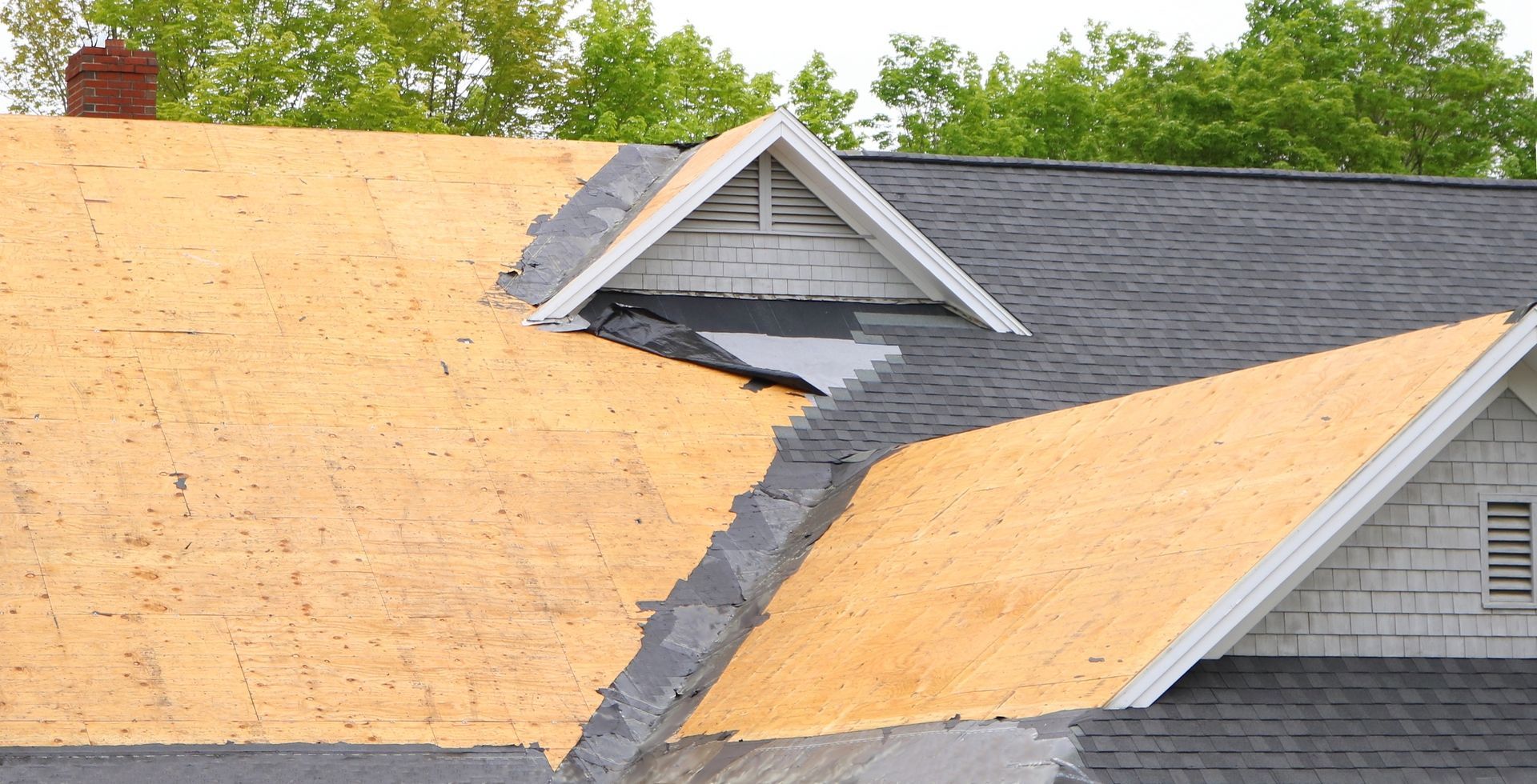 Damaged roof with exposed plywood and a large dark tear through the shingles