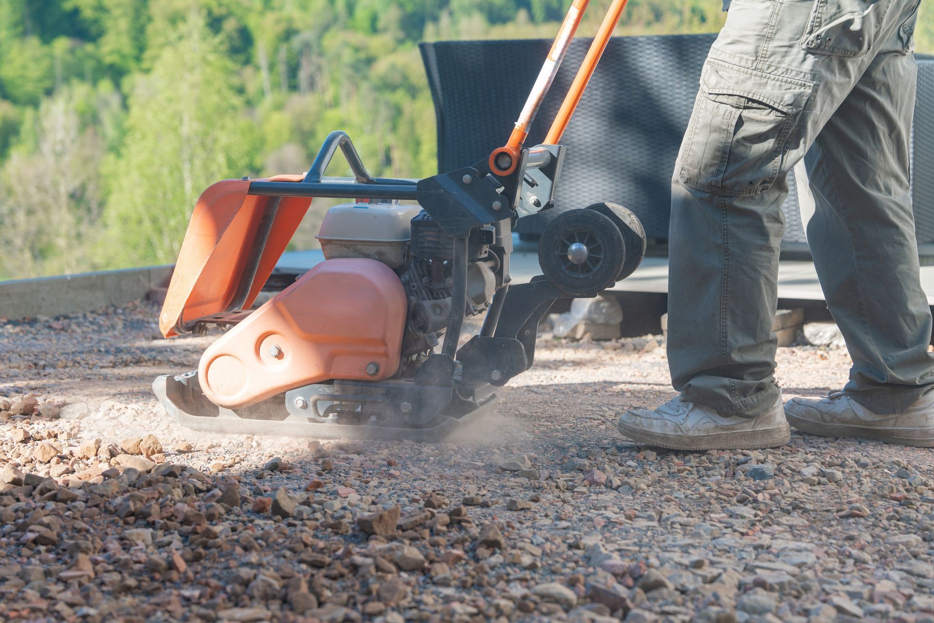 Worker using a red chain trencher to cut gravel road edges outdoors.