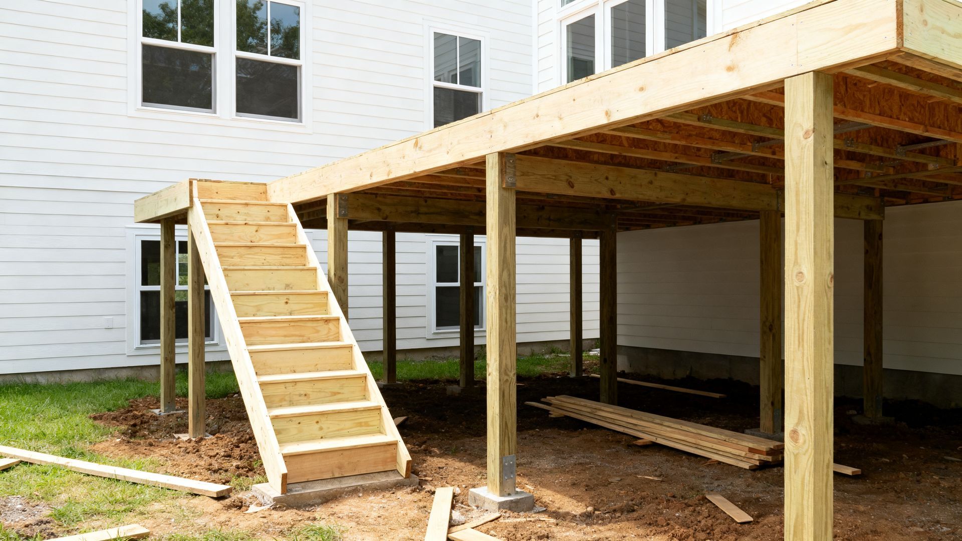 Wooden accessibility ramp leading to an elevated deck beside a white house