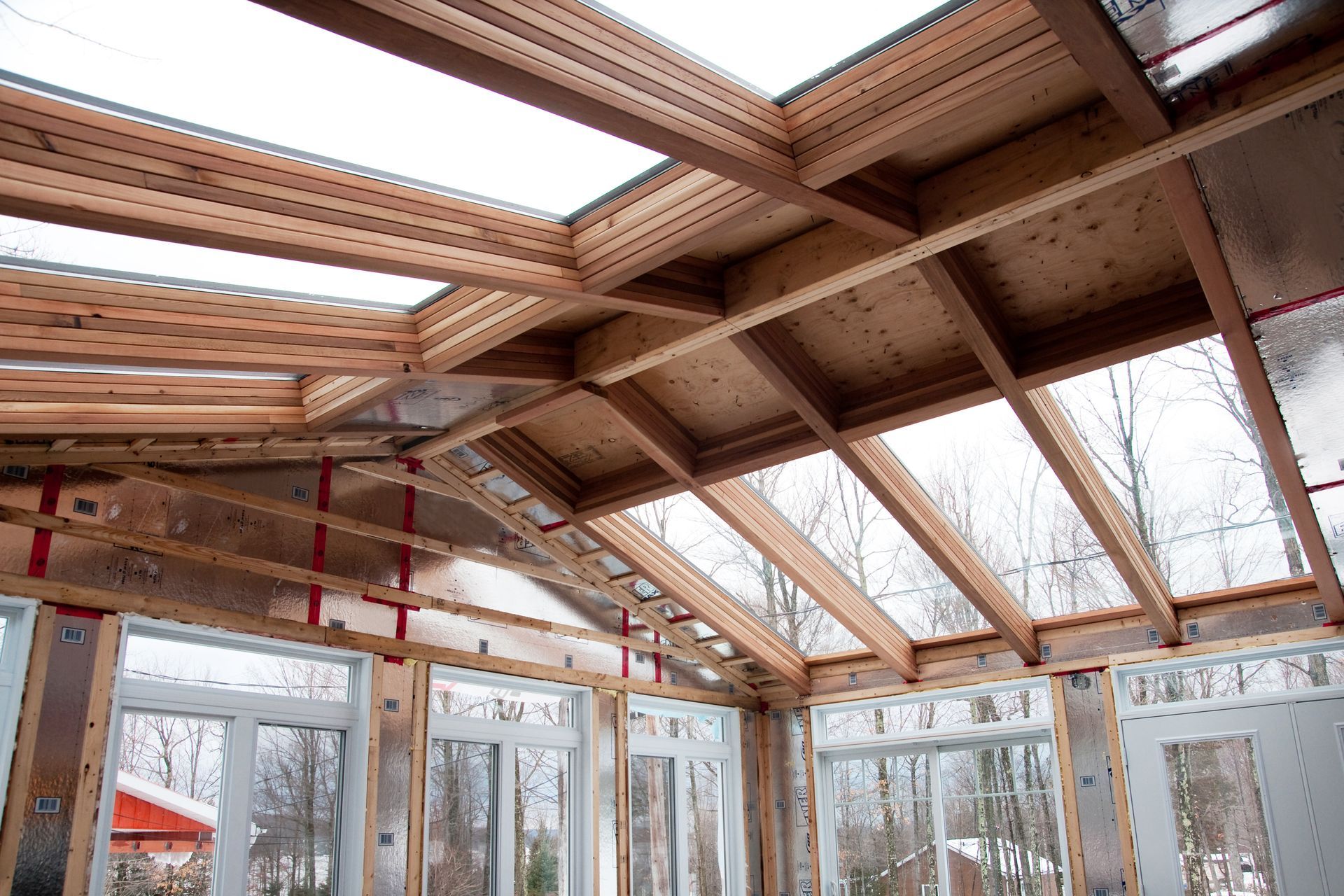 Interior of a glass sunroom under construction with exposed wooden roof beams and red support poles