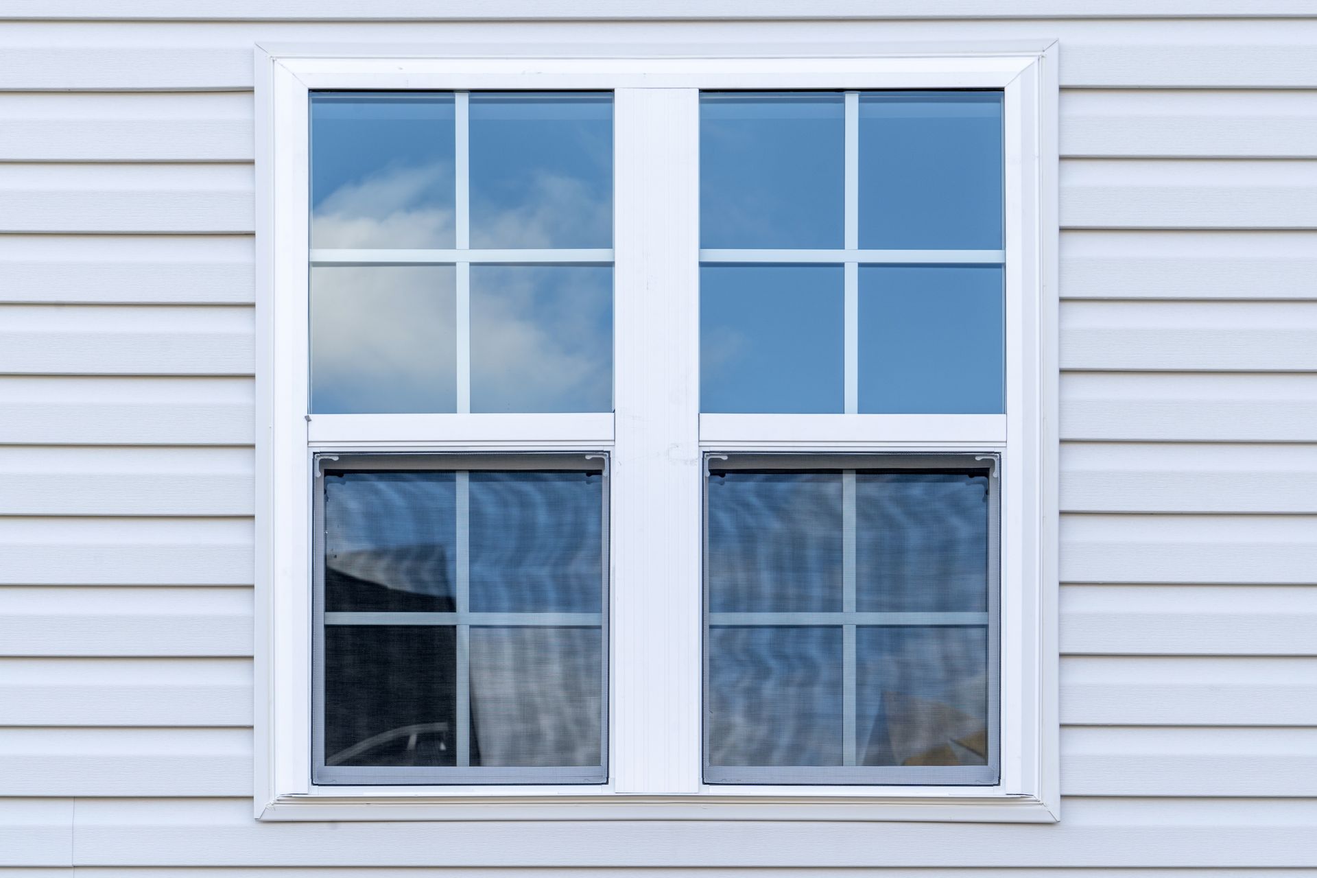 A white window on the side of a house with a blue sky reflected in the window.