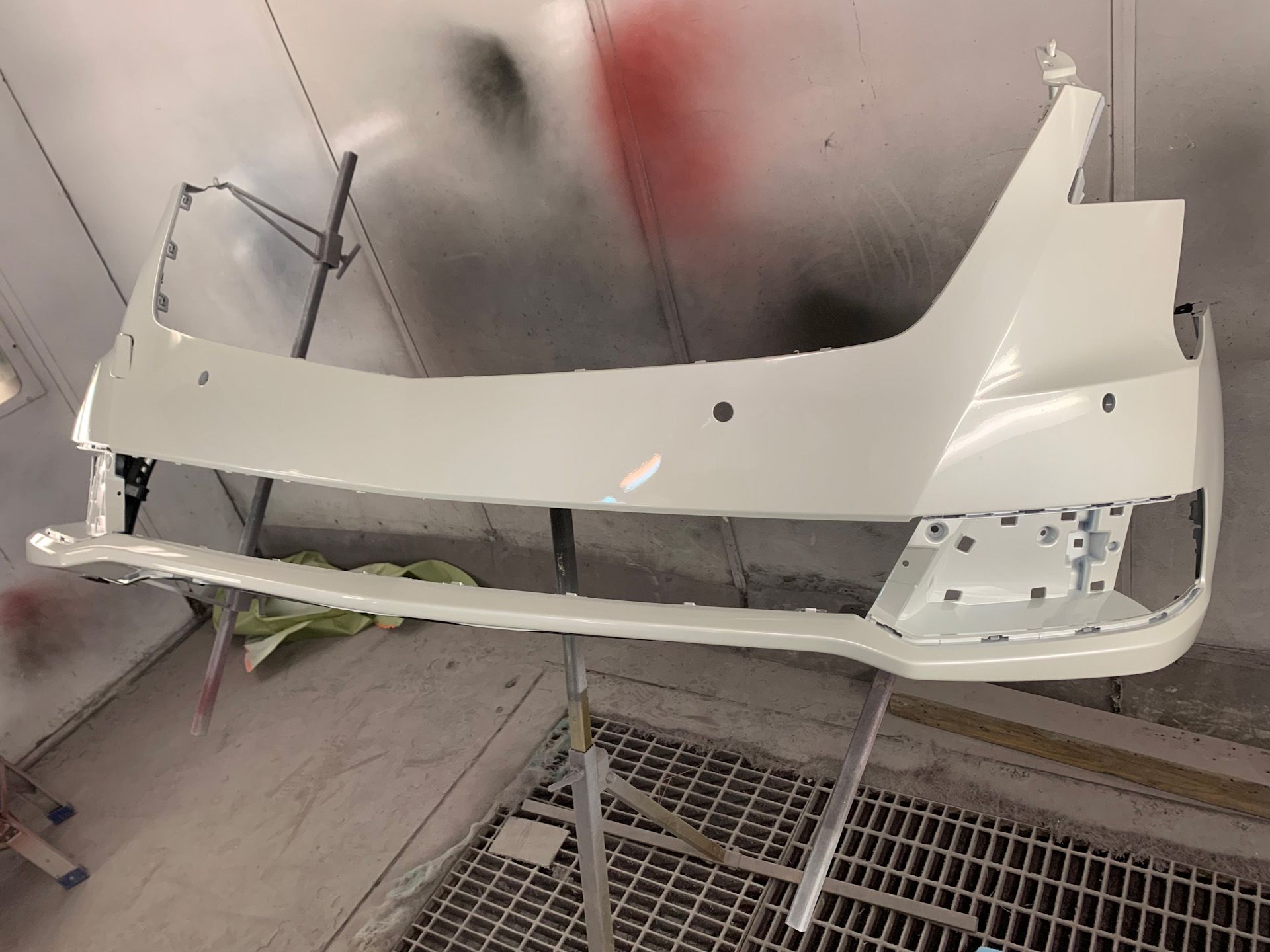 A white car bumper is being painted in a paint booth.