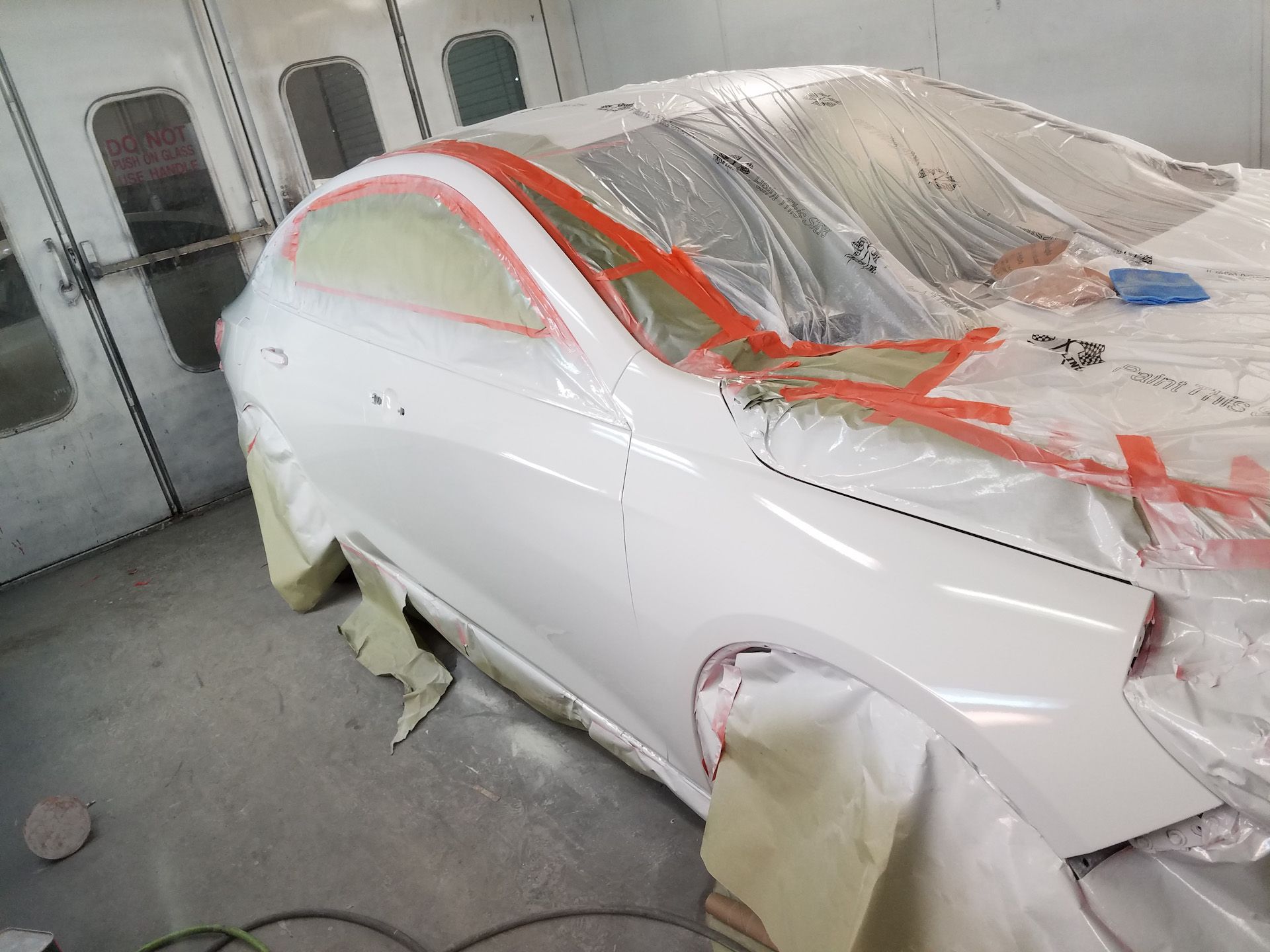 A white car is being painted in a paint booth.