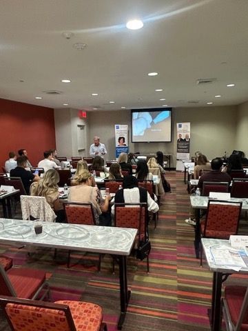 Conference room with seated audience facing a presentation screen and speakers at the front