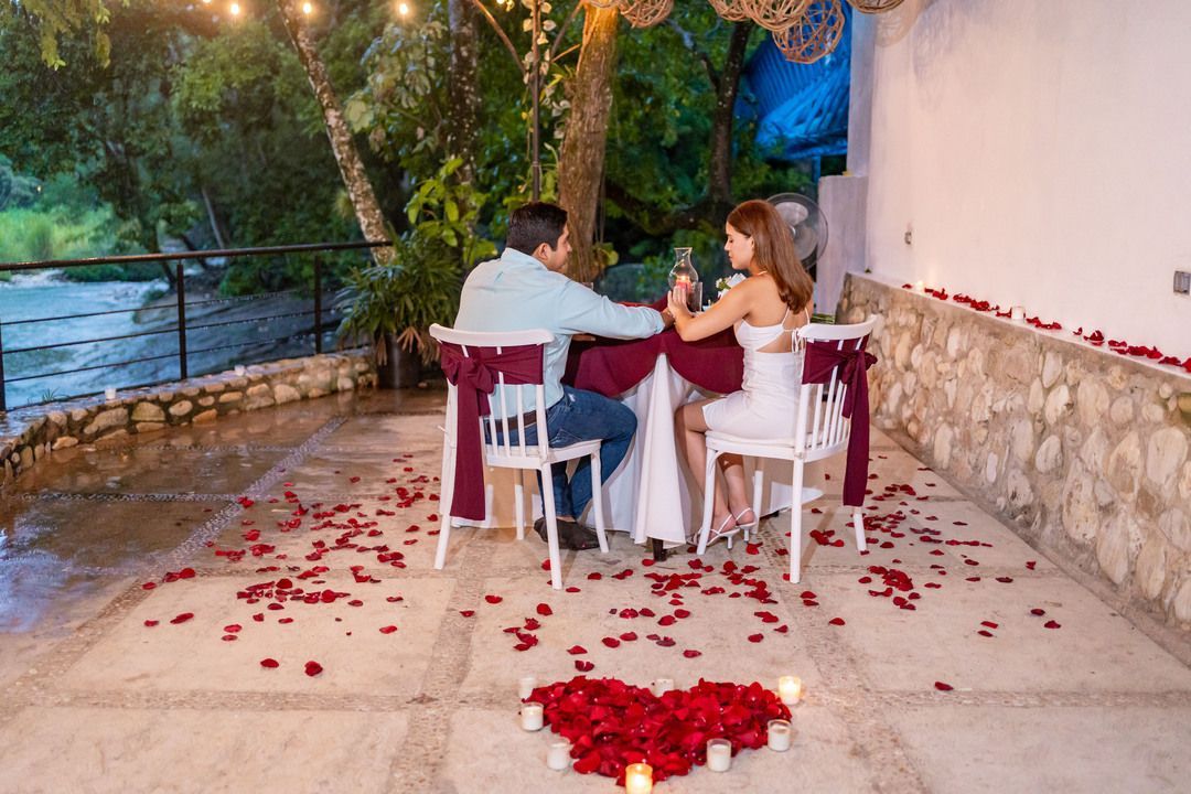 Un hombre y una mujer están sentados en una mesa decorada con pétalos de rosa y velas.