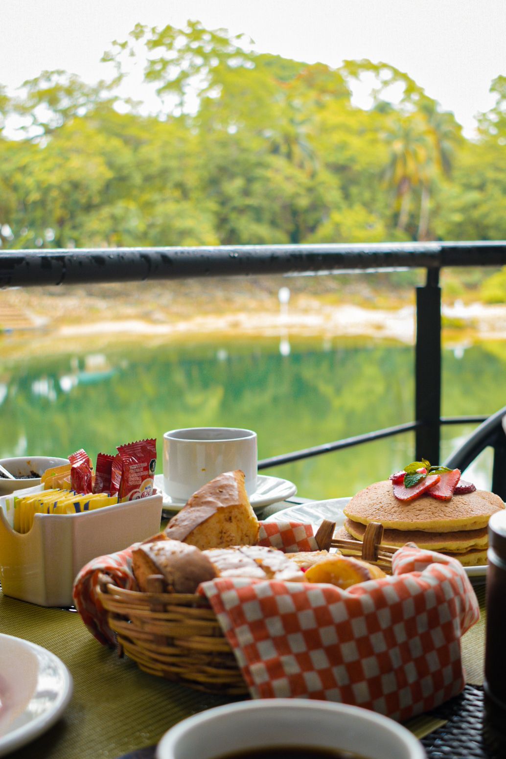 Una mesa cubierta de panqueques, pan y café con vista a un lago.