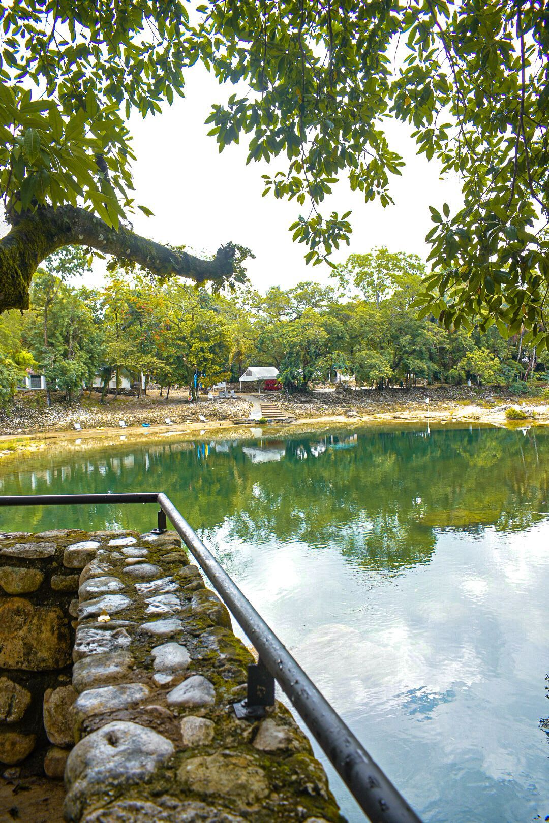Un muro de piedra que conduce a un lago rodeado de árboles.