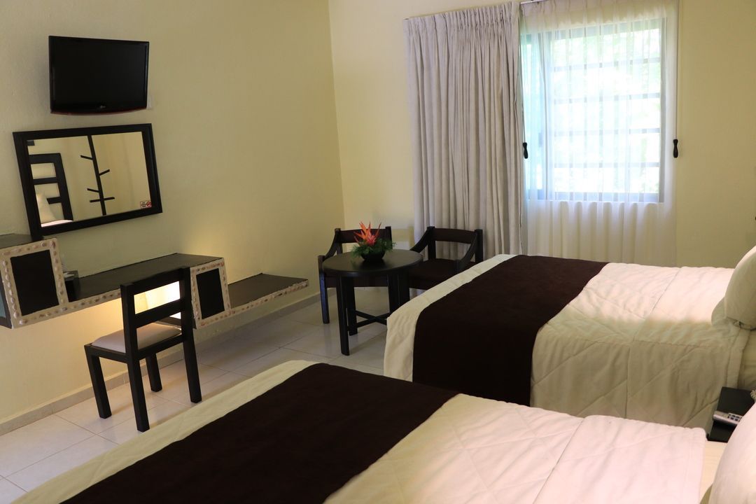 Una habitación de hotel con dos camas, una mesa, sillas y un televisor de pantalla plana.