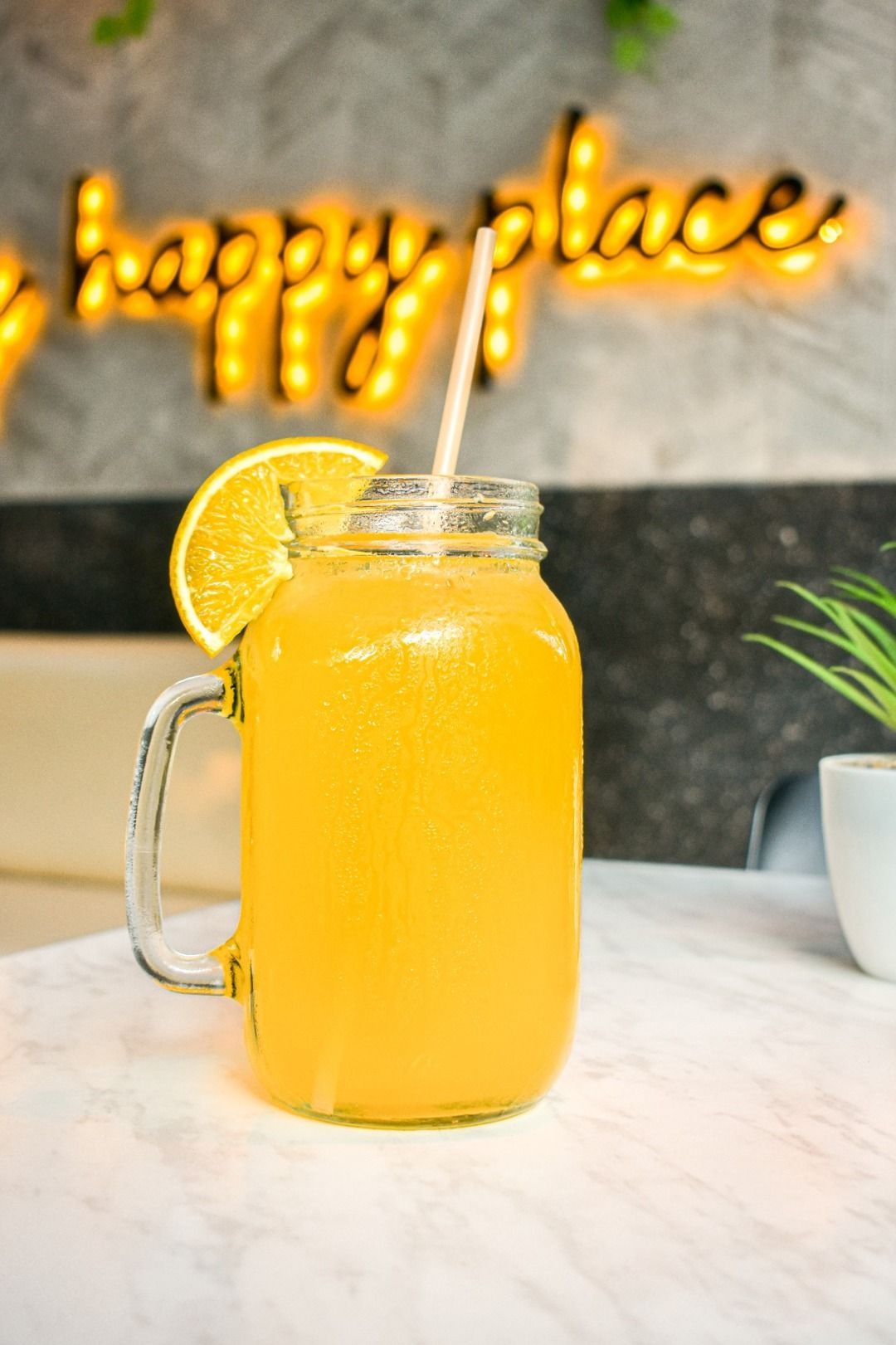 Un frasco de vidrio lleno de jugo de naranja y una pajita sobre una mesa.