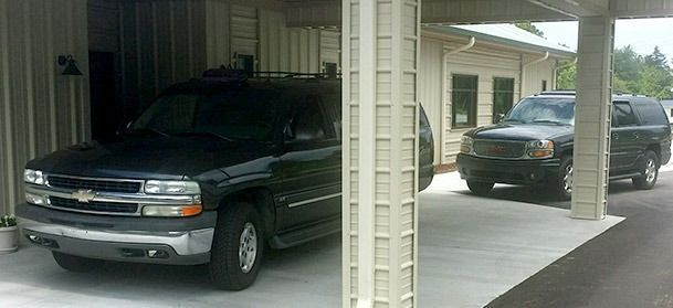 Two black SUVs parked under covered structures.