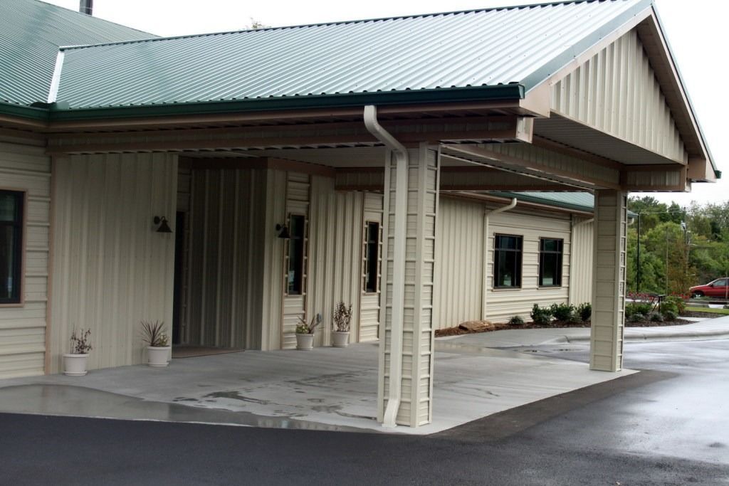 Exterior of a building with light beige siding and a covered entry with green corrugated metal roof.